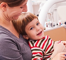 Mother holding young child in lap at dentist