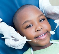 A young boy smiling while a dentist prepares to check and clean his teeth