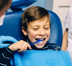 A little boy brushing his teeth in the dentist chair