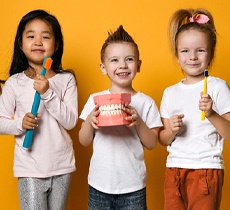 Three children standing together holding toothbrushes and a mold of a mouth