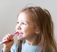 Child smiling while brushing her teeth
