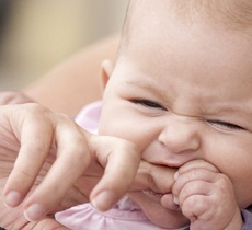A baby holding its parent’s finger and chewing on it to relieve discomfort caused by teething