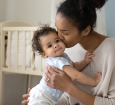 A mother holding her baby and kissing it on the cheek