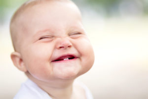 A smiling infant with two bottom teeth 