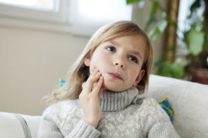 a young child wearing a sweater and holding her jaw in pain 