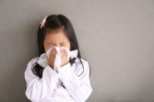 Little girl in white polka dotted shirt blowing her nose into a tissue